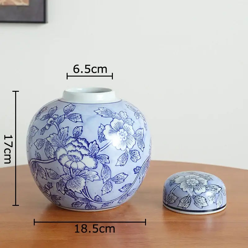 A round light blue ceramic tea caddy with dark blue floral patterns next to a white porcelain vase for living room decor