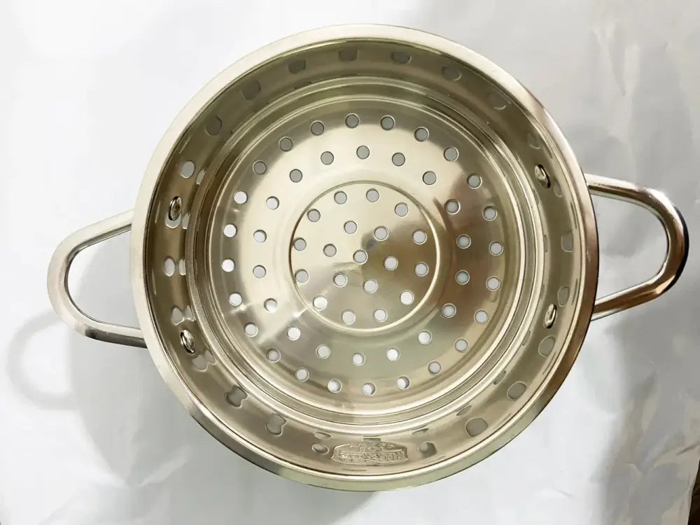 Shiny stainless steel steamer basket with two handles and circular holes for use with flower edged baby food pot set