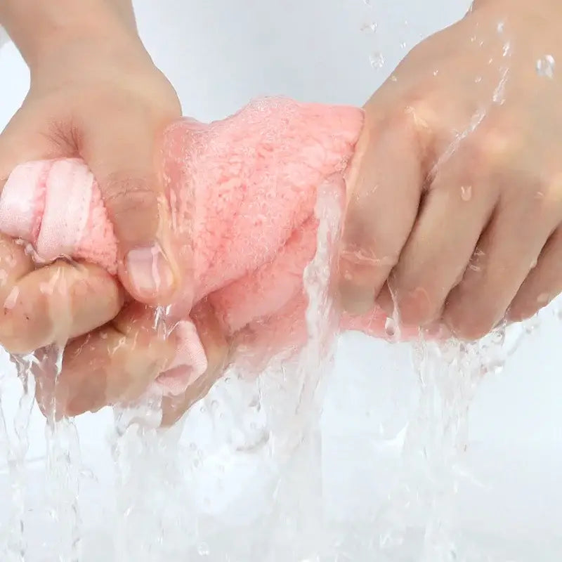Pink textured sponge being squeezed in water with flower shaped pink and light blue decorbites coral fleece hand towels