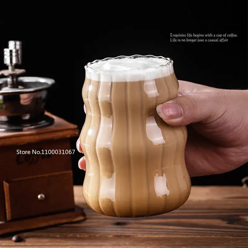A clear ribbed glass coffee mug with fluted rim and handle filled with frothy latte in glass coffee mug set