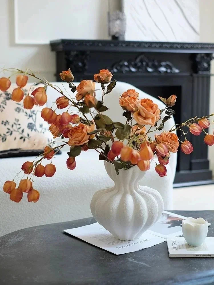 White ceramic fluted vase with bulbous body and narrow neck holding dried orange roses and golden lantern flowers