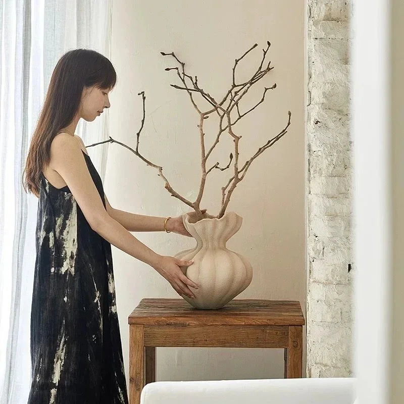 Cream-colored ceramic vase with fluted sculpted body and wide opening holding bare branches for minimalist decor
