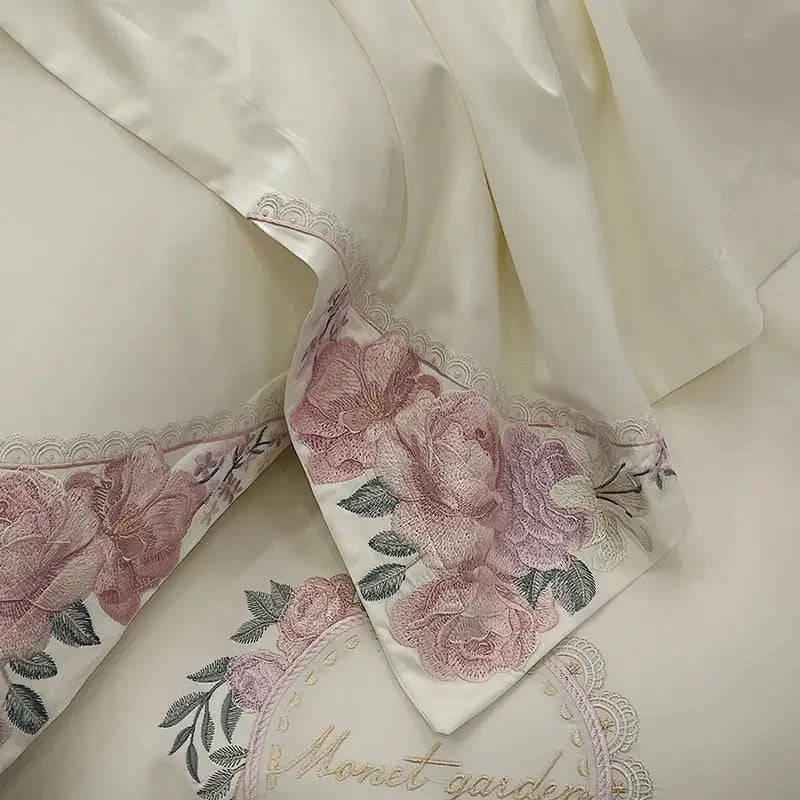Cream-colored satin pillowcase with pink and green french flowers embroidery and lace trim in a luxury bedding set