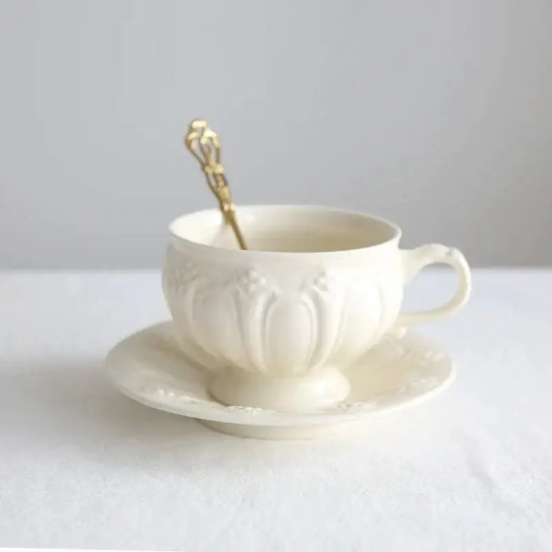 A delicate french garden cream porcelain tea cup with floral embossing on a matching saucer and ornate gold spoon