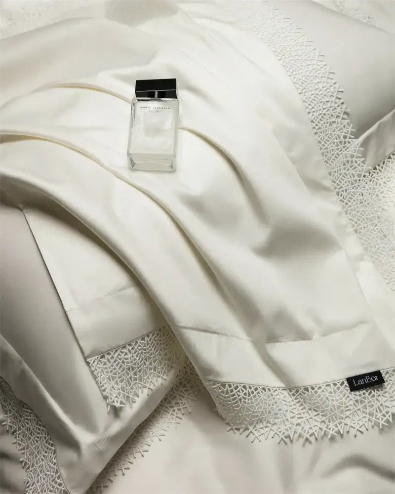 A clear glass perfume bottle with black cap labeled narciso rodriguez shown alongside french lace edge white silver bedding set decorbites