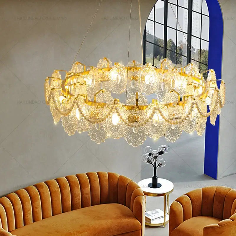 A luxurious gold-toned decorbites glass chandelier with crystal droplets above an orange velvet sofa