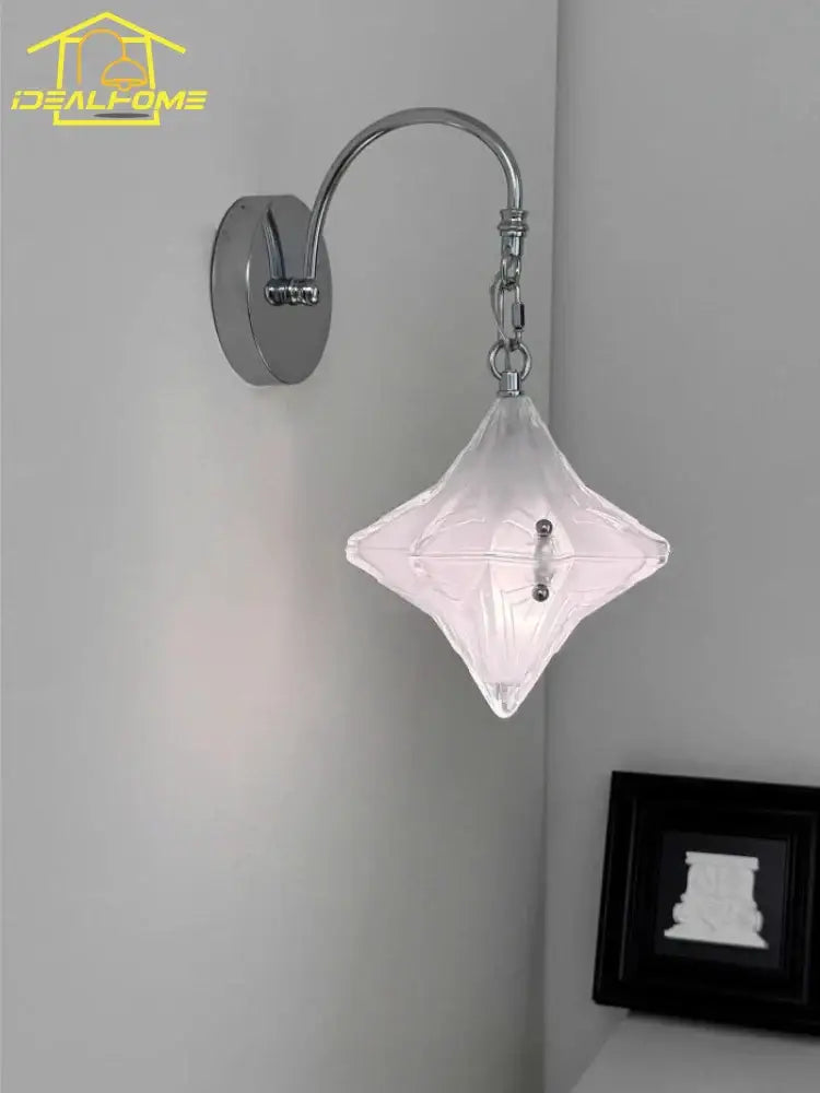 A clear diamond-shaped glass wall lamp with chrome french medieval bauhaus curved arm for living room use