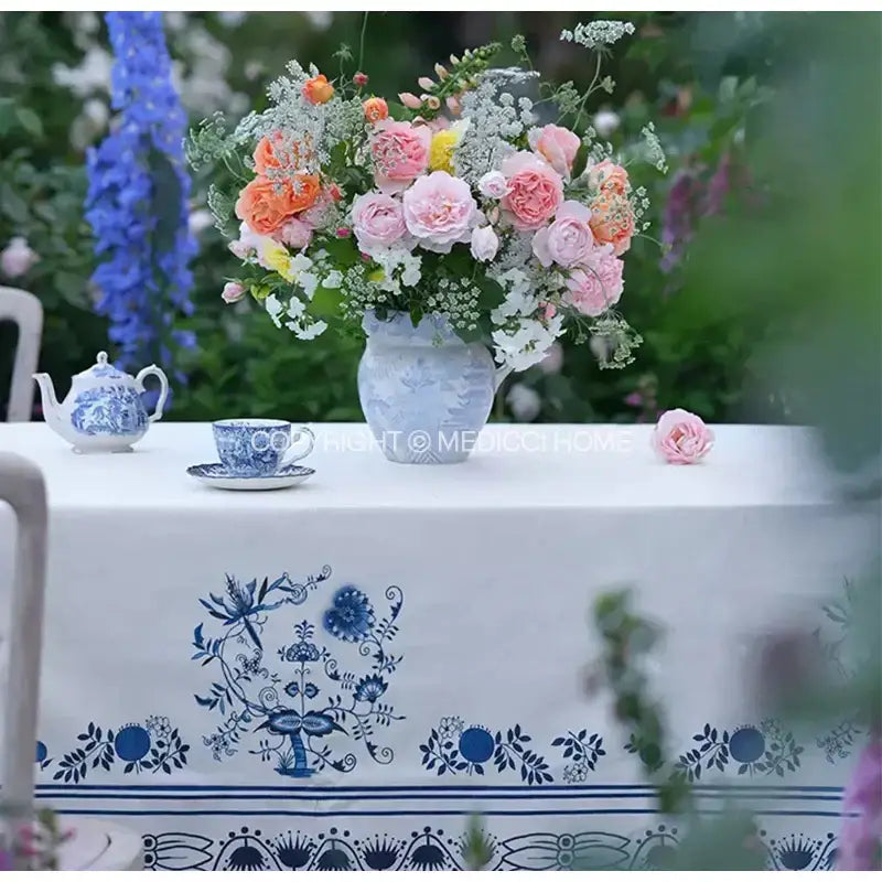 A blue and white ceramic vase with floral pattern holding pink orange yellow white flowers on a decorbites blue onion print tablecloth