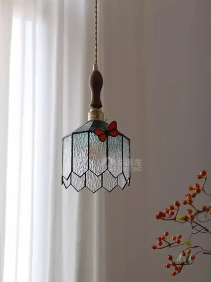 A delicate hexagonal blue-green textured stained glass decorbites butterfly chandelier with red butterfly motif and dark wood chain