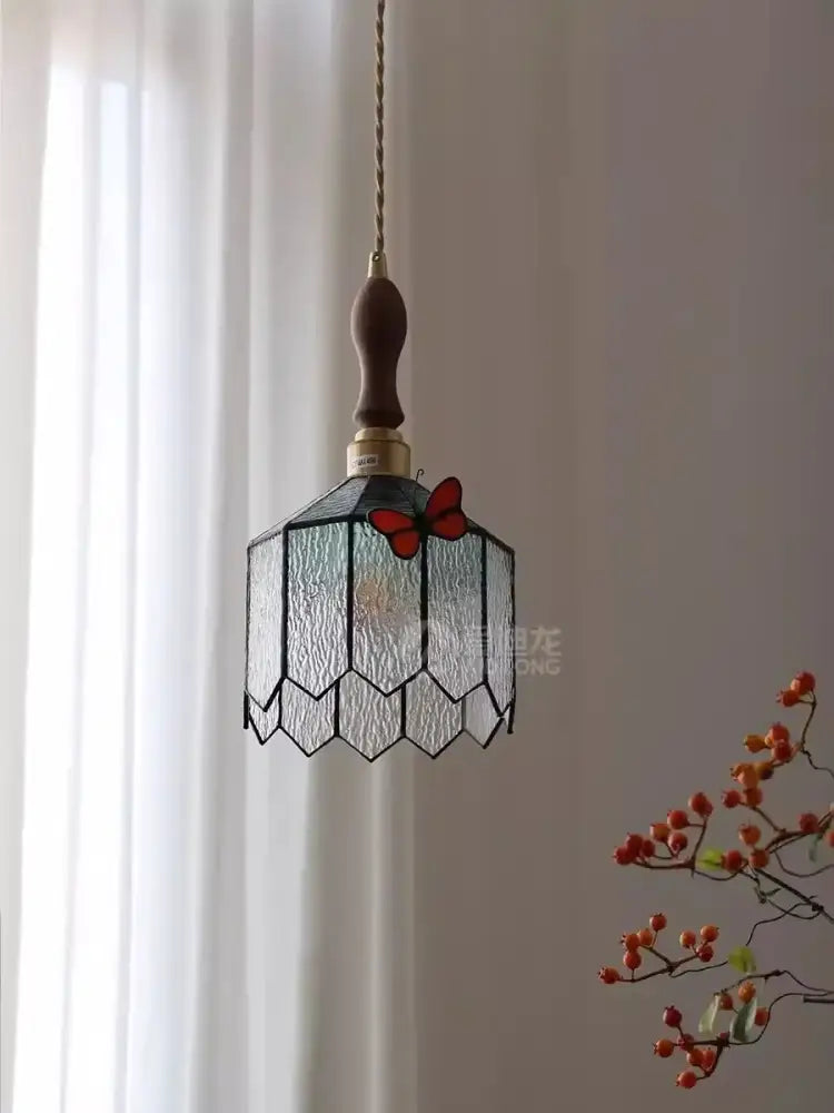 A delicate hexagonal blue-green textured stained glass decorbites butterfly chandelier with red butterfly motif and dark wood chain