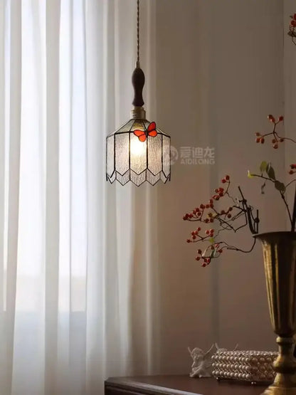 A warm-toned hexagonal stained glass decorbites butterfly chandelier with red butterfly accent and dark metal frame