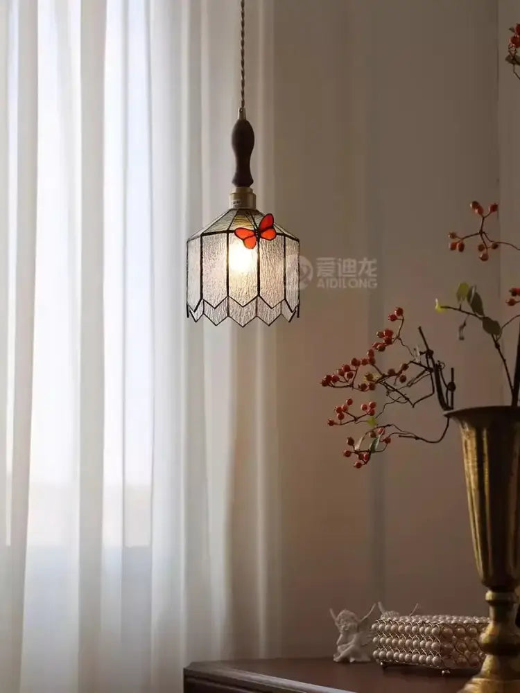 A warm-toned hexagonal stained glass decorbites butterfly chandelier with red butterfly accent and dark metal frame