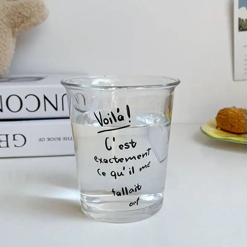 Clear glass tumbler cup filled with water featuring handwritten french text in black marker for kitchen use
