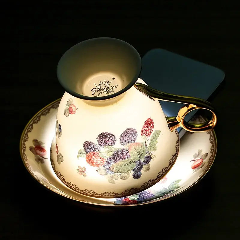 A cream-colored bone china tea cup with gold trim and hand-painted berry design from a French style teaware set