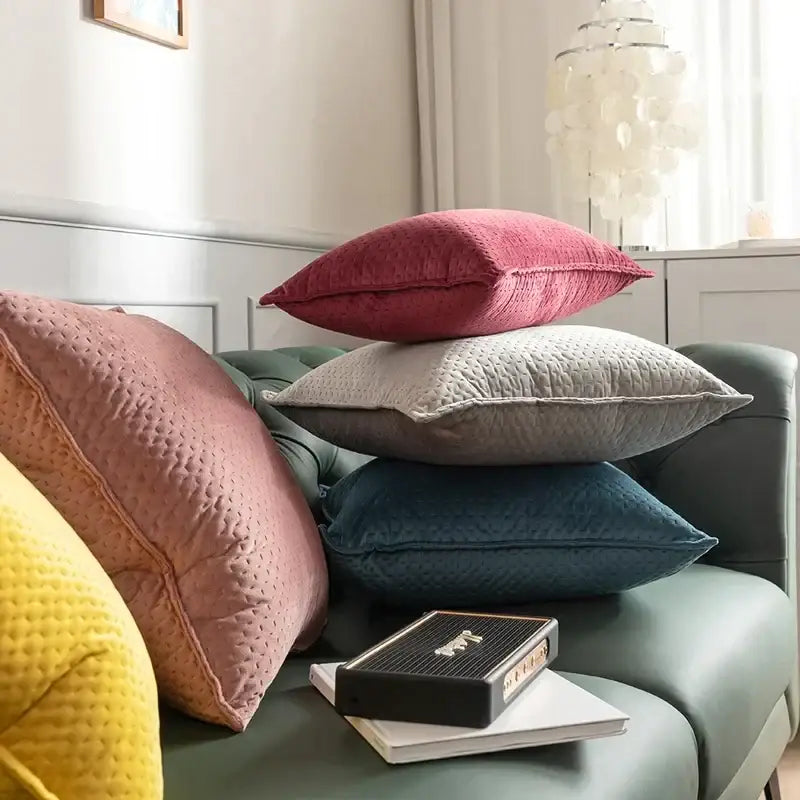 Stack of decorbites fringed velvet cushion covers in muted pink gray and teal on a green sofa for living room decor