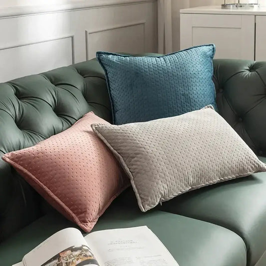 Three quilted dot patterned fringed velvet cushion covers in dusty rose muted blue and beige on a green sofa