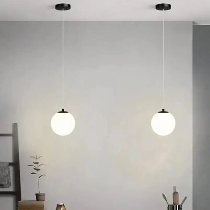 Two minimalist frosted glass pendant lights with spherical white shades and black fixtures for dining room use