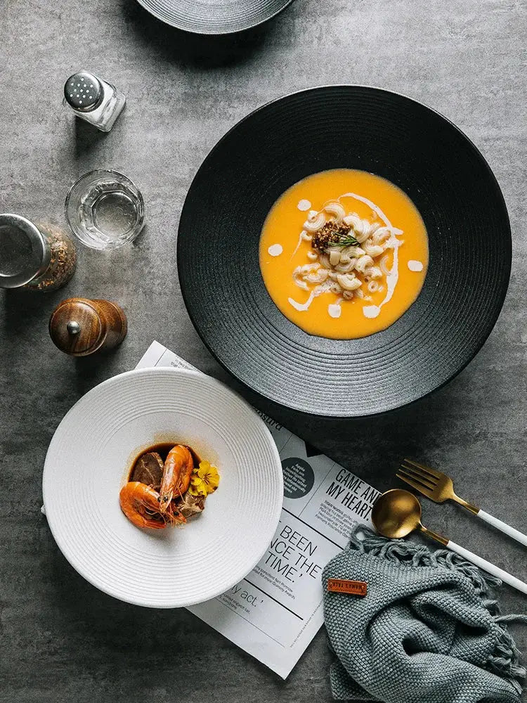 Black ceramic bowl with textured rim holding orange soup garnished with pasta and cream from decorbites frosted glaze ceramic set