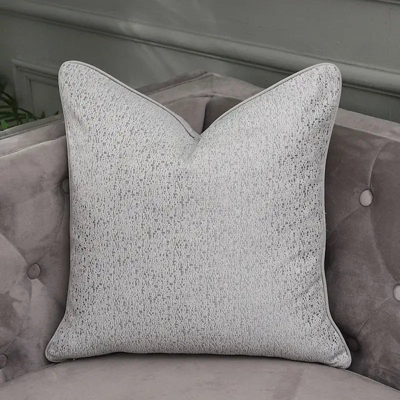 A square light gray textured throw pillow with subtle speckled pattern and piping for decorbites frosted gold pillow covers