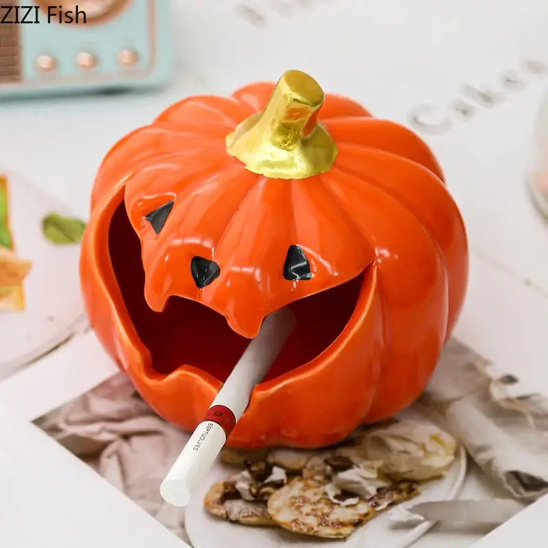 Vibrant orange ceramic halloween pumpkin ghost ashtray with shiny gold stem and carved mouth holding a cigarette
