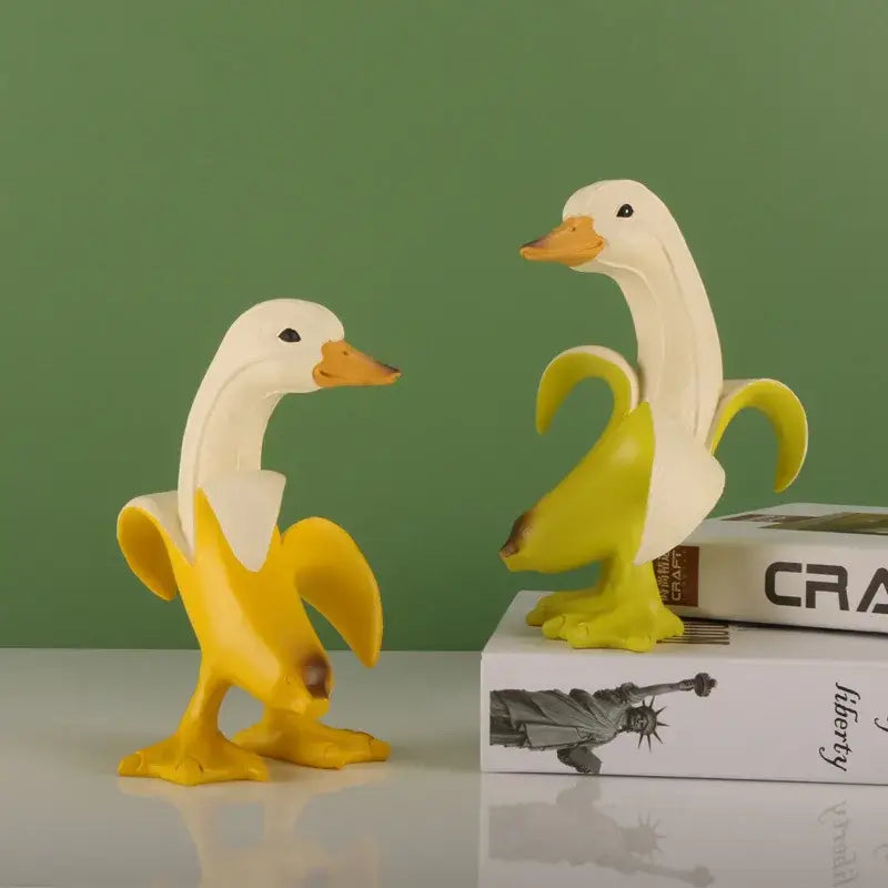 Two whimsical white resin duck sculptures with orange beaks wrapped in bright yellow banana peels banana duck sculpture