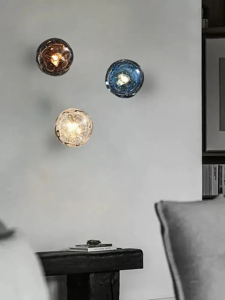 Three spherical glass wall sconce lamps in amber deep blue and frosted gold with crackled textured surfaces for living room lighting