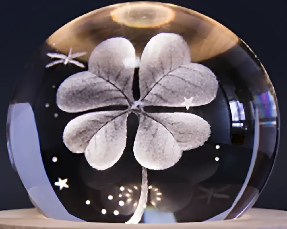 A clear spherical crystal ball music box with an etched four-leaf clover and star patterns on a wooden base