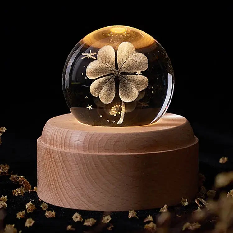 A glowing crystal ball music box with a golden four-leaf clover design on a light wood rotating base