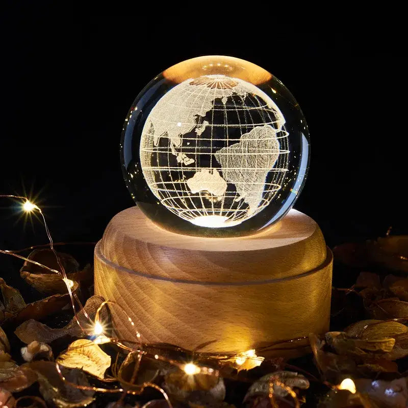 A clear crystal ball music box with engraved globe and warm wooden base emits a soft rotating light glow for bedroom use