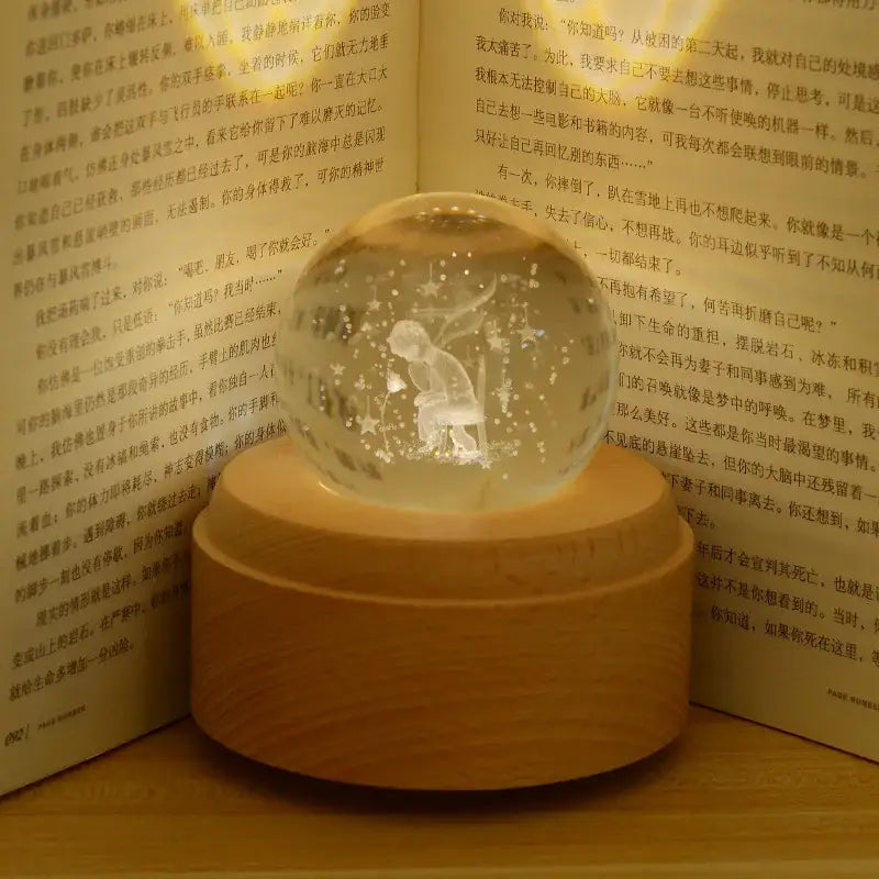 A translucent glass crystal ball music box with golden base featuring illuminated child and stars scene rotating light glow
