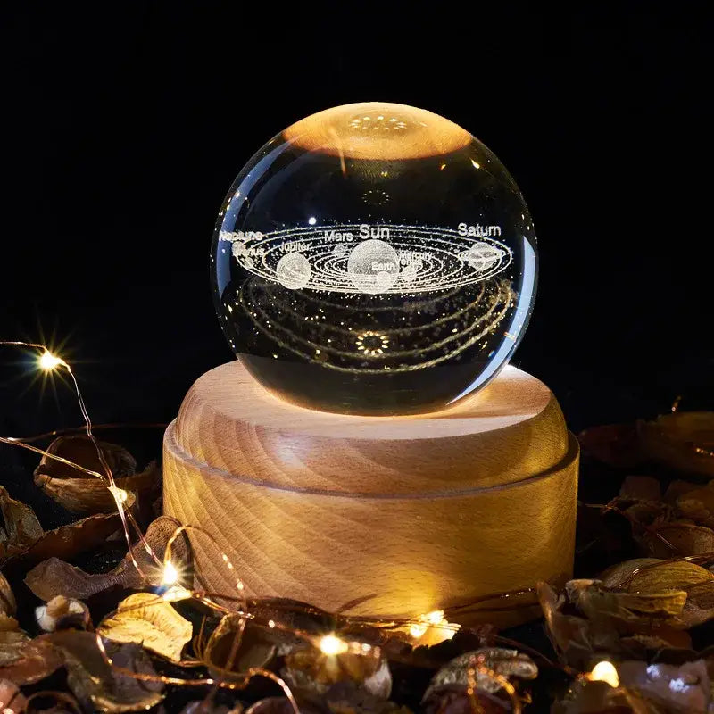 A clear spherical crystal ball music box with engraved solar system design featuring labeled planets and orbits