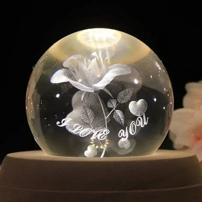 A clear spherical crystal ball music box with engraved rose and illuminated i love you message rotating wooden base