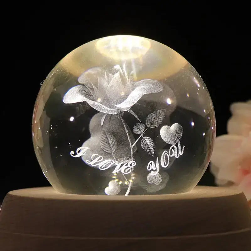 A clear spherical crystal ball music box with engraved rose and illuminated i love you message rotating wooden base
