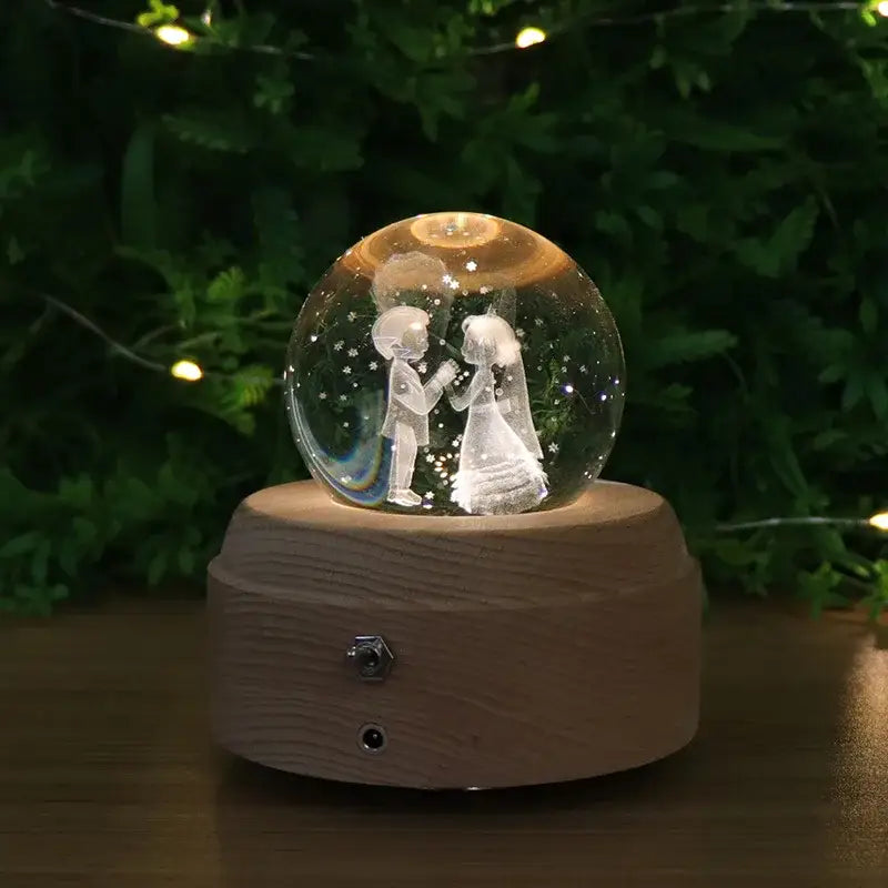 A clear crystal ball music box with an engraved dancing couple inside on a light brown wooden base