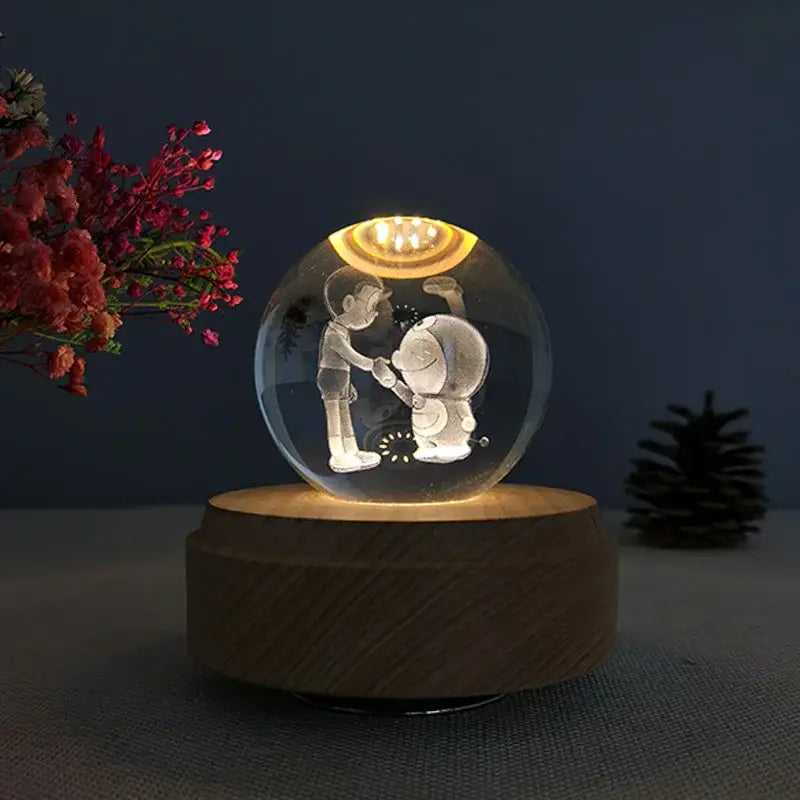 A clear glass crystal ball music box with laser-engraved characters illuminated by warm led lights on a wooden base