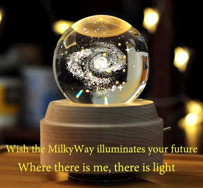 A clear glass crystal ball music box with a swirling galaxy design and stars on a wooden rotating base