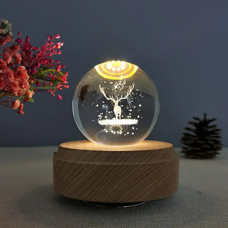 A glowing crystal ball music box with engraved deer design and warm yellow light on a wooden rotating base