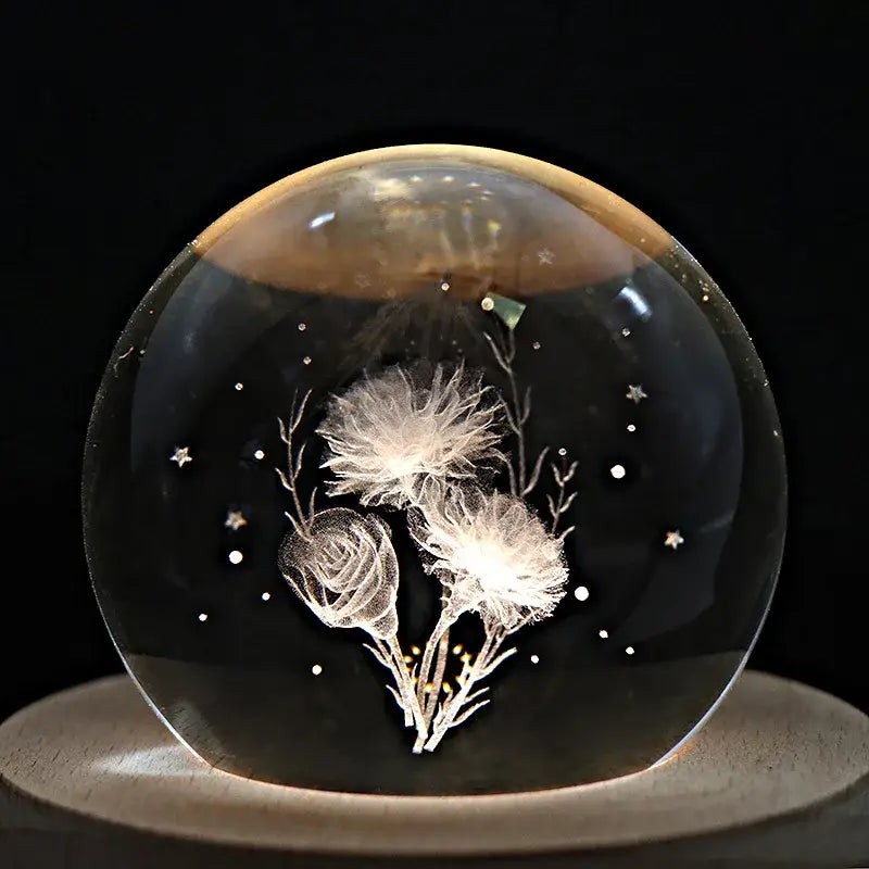 A clear crystal ball music box with etched white dandelion and rose blossoms on a rotating wooden base