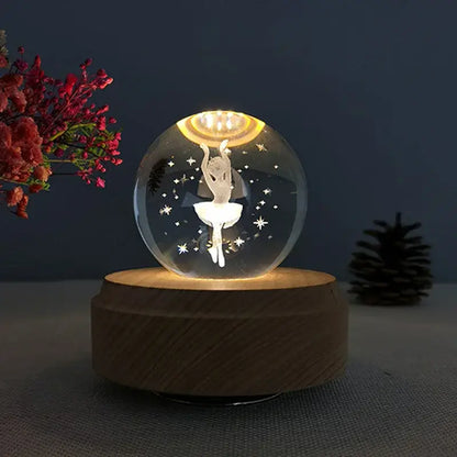 A clear glass crystal ball music box with a white ballerina silhouette and star cutouts glowing on a wooden base