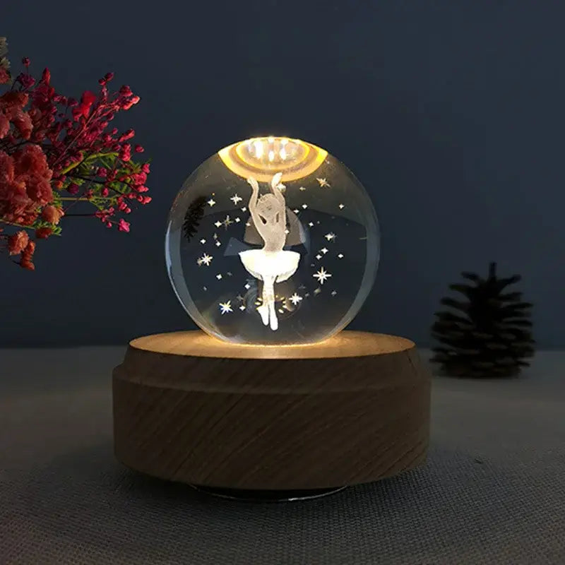 A clear glass crystal ball music box with a white ballerina silhouette and star cutouts glowing on a wooden base