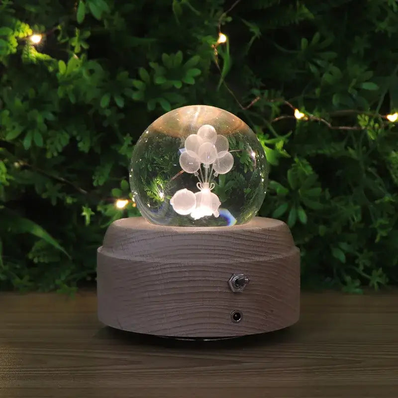 A clear glass crystal ball music box with a white balloon figure on a wooden rotating base glowing in bedroom light
