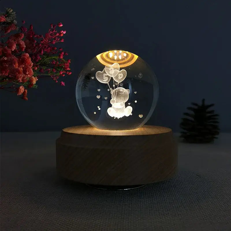 A clear crystal ball music box with an engraved teddy bear and warm rotating light on a wooden base