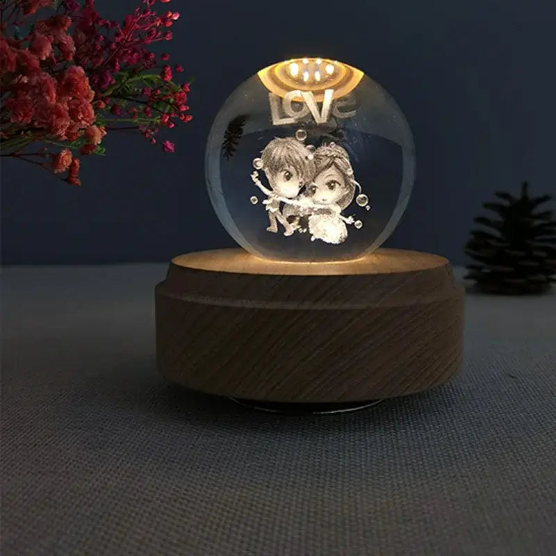 A clear crystal ball music box with a laser-engraved couple and love text illuminated by warm led light