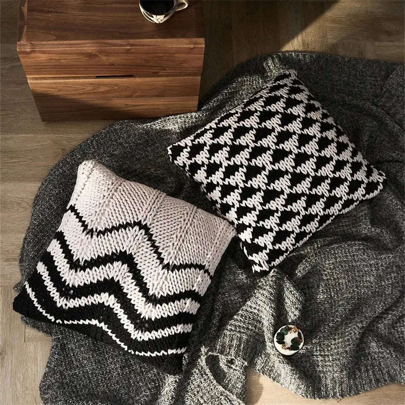 Two geo knit stripe square pillows in black white and cream black resting on a gray knit blanket for decorbites geo knit decor