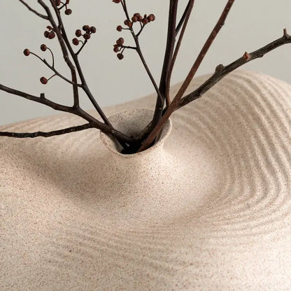 Beige speckled geometric abstract ceramic vase with concentric ripple texture holding dark berry branches for living room decor