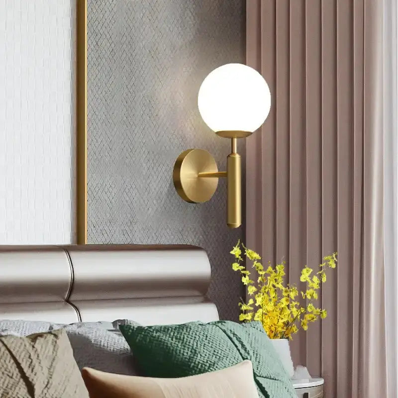 Gold-toned spherical wall sconce with frosted glass globe complementing geometric amber and cream glass pendant light for dining room