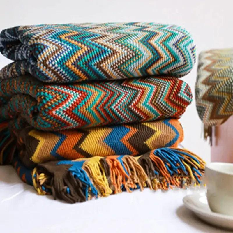 Stacked woven geometric aztec baja throw blankets in teal orange brown and blue with fringed edges for living room decor
