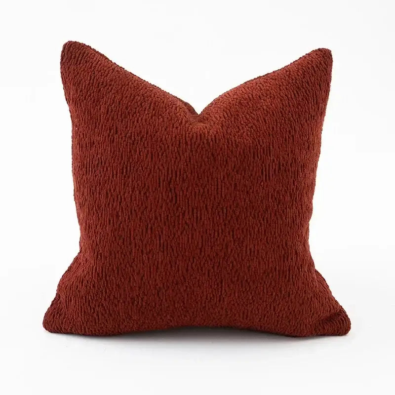 A rust-colored square throw pillow with plush textured fabric from a geometric black and cream pillow cover set for living room