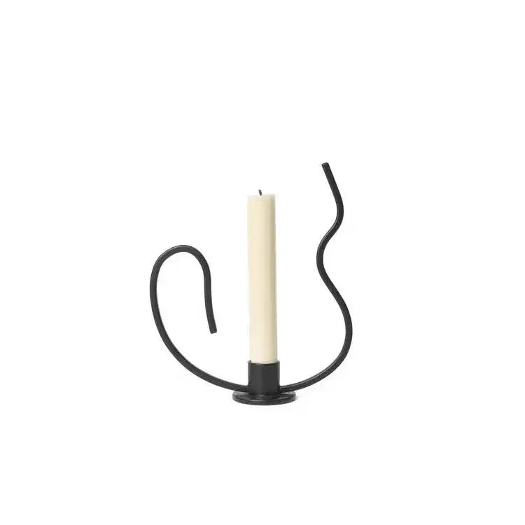 Geometric black metal candlestick candelabrum with flowing wrought iron curves holds a single off-white pillar candle