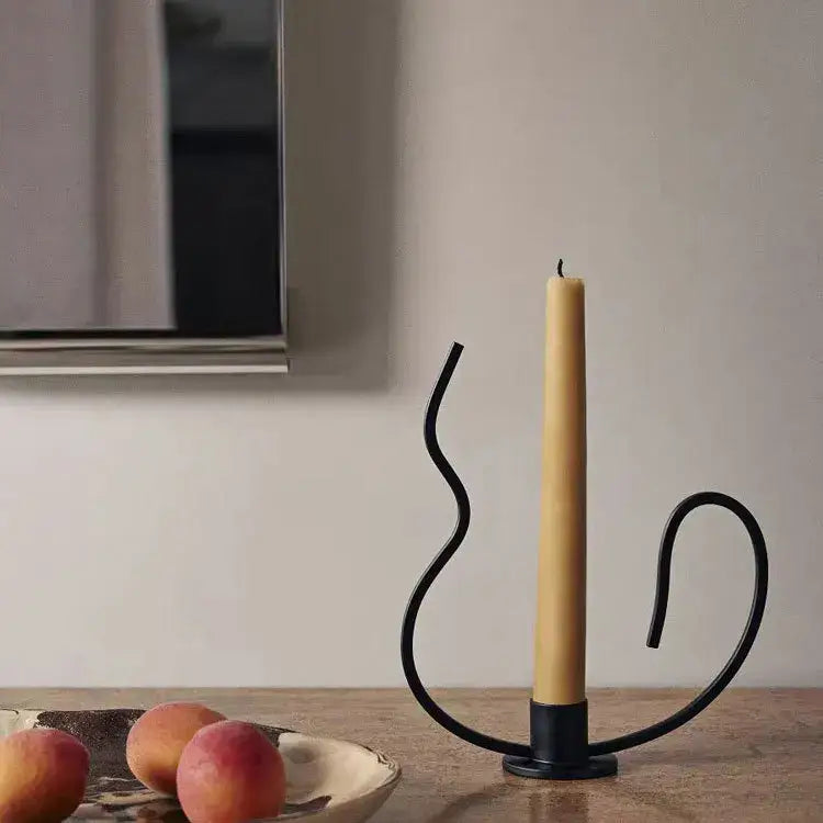 Black wrought iron candlestick candelabrum with geometric black curved design holding a tall yellow candle centerpiece